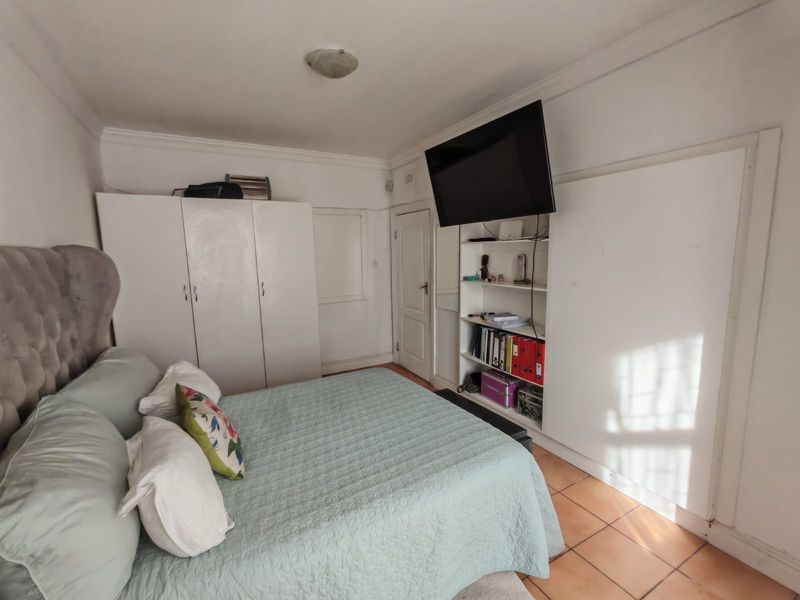 A functional bedroom featuring built-in cupboards, integrated shelving, and tiled flooring, offering a practical layout with potential for cosmetic updates.
