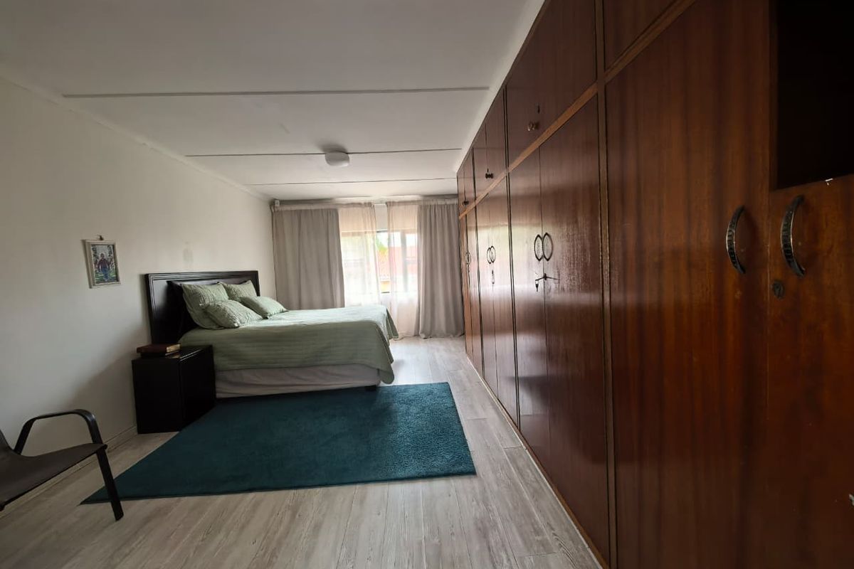 Spacious bedroom featuring extensive floor-to-ceiling built-in wooden cabinetry, light-toned wood-look flooring, and large windows allowing for natural light.