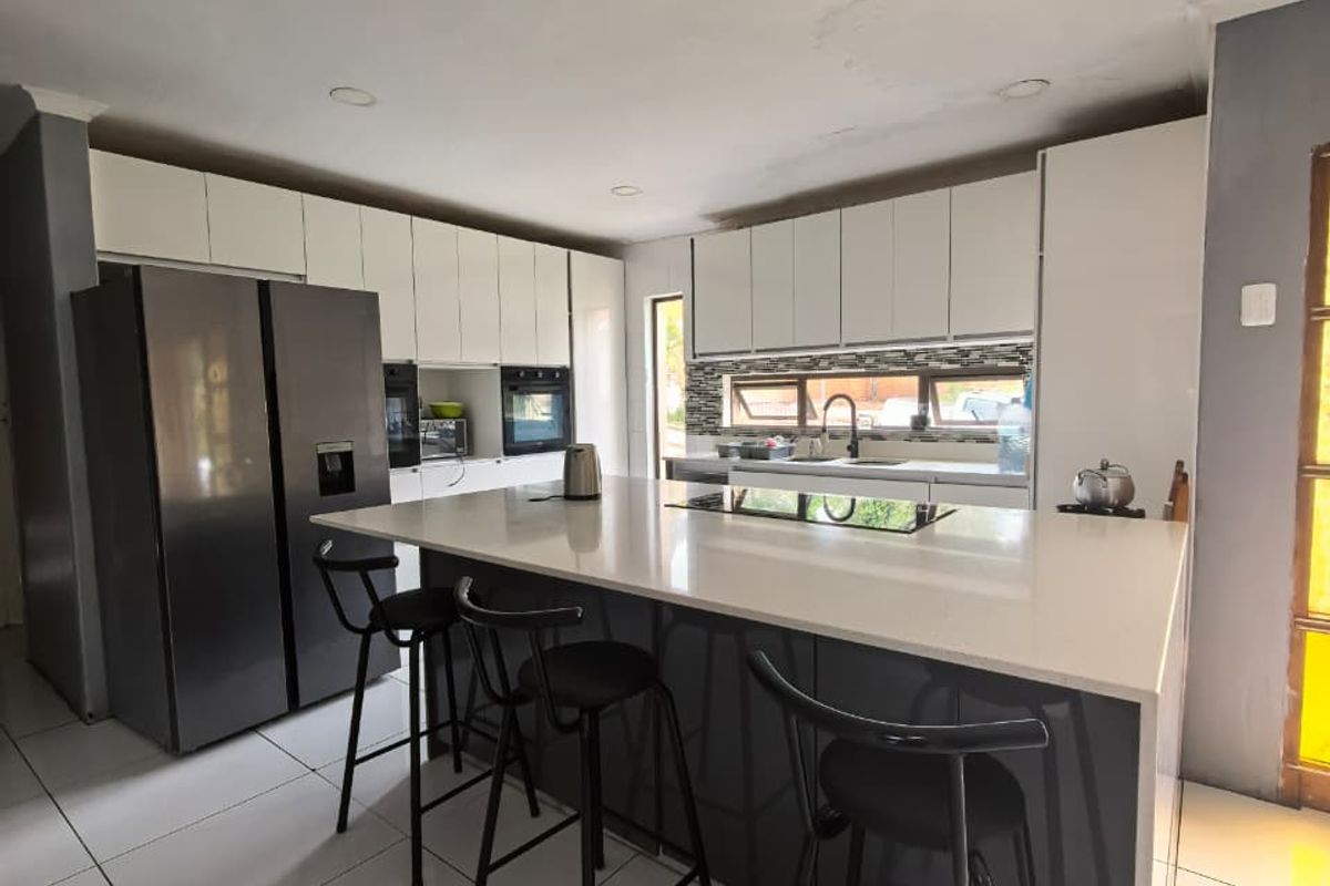 Modern kitchen featuring a large central island with stone countertops, sleek white cabinetry, built-in oven, and tiled flooring.
