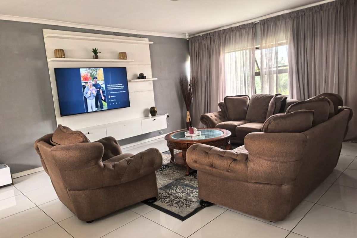 A comfortable living room featuring large format floor tiles, a built-in media wall unit, and expansive windows with curtain treatments.