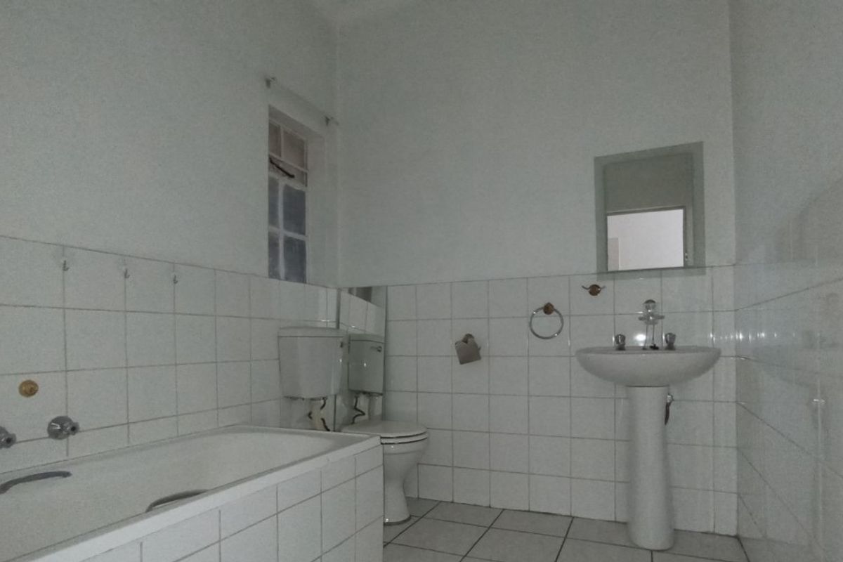 A functional, tiled bathroom featuring a pedestal washbasin, a standard bathtub, and a toilet, offering a clean and neutral space ready for updates.