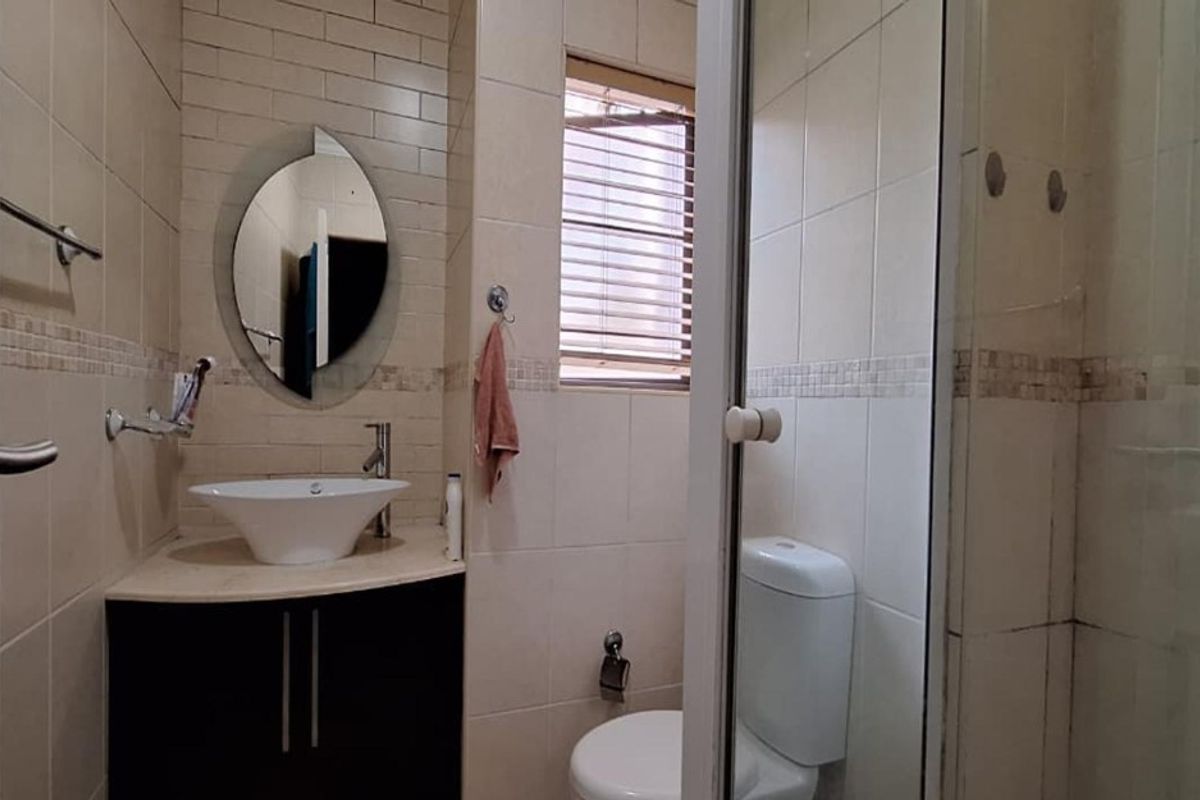 Compact bathroom featuring a vessel sink on a vanity cabinet, a toilet, and a glass-enclosed shower with neutral wall tiling.