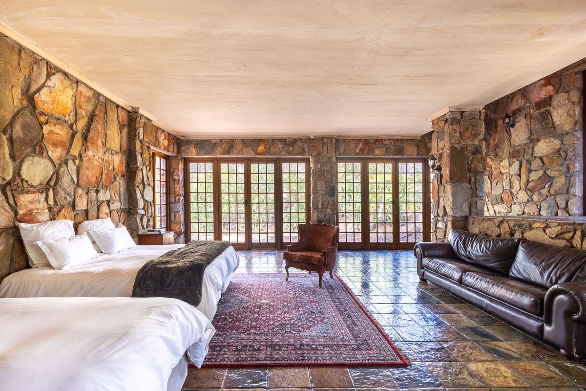 Spacious bedroom featuring rustic stone walls, tiled flooring, and multiple sets of French doors providing natural light and garden access.