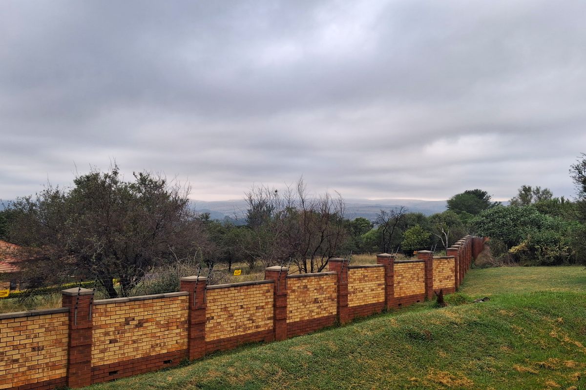 A view of a residential property boundary featuring a sturdy brick wall with integrated electric fencing, overlooking a natural landscape.