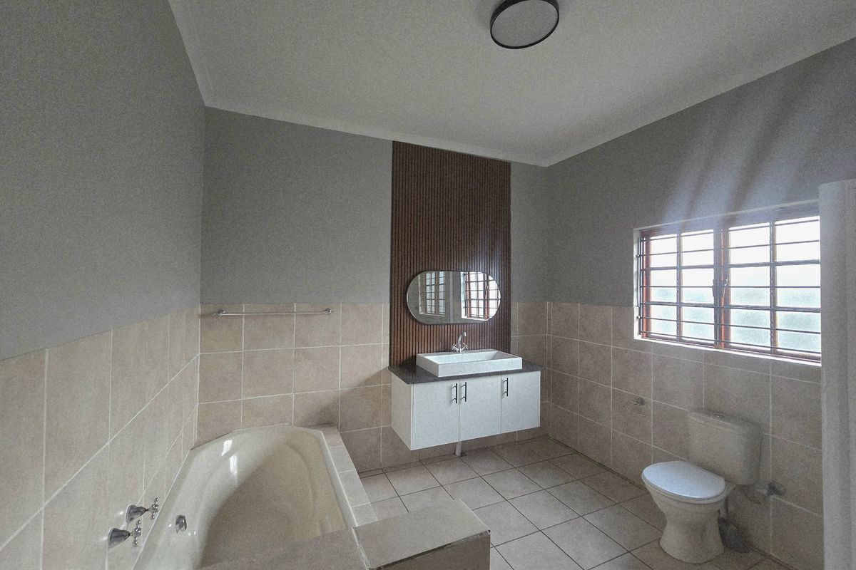 A clean, empty bathroom featuring a built-in bathtub, a modern vanity with a vessel sink, and a decorative slatted wood feature wall.