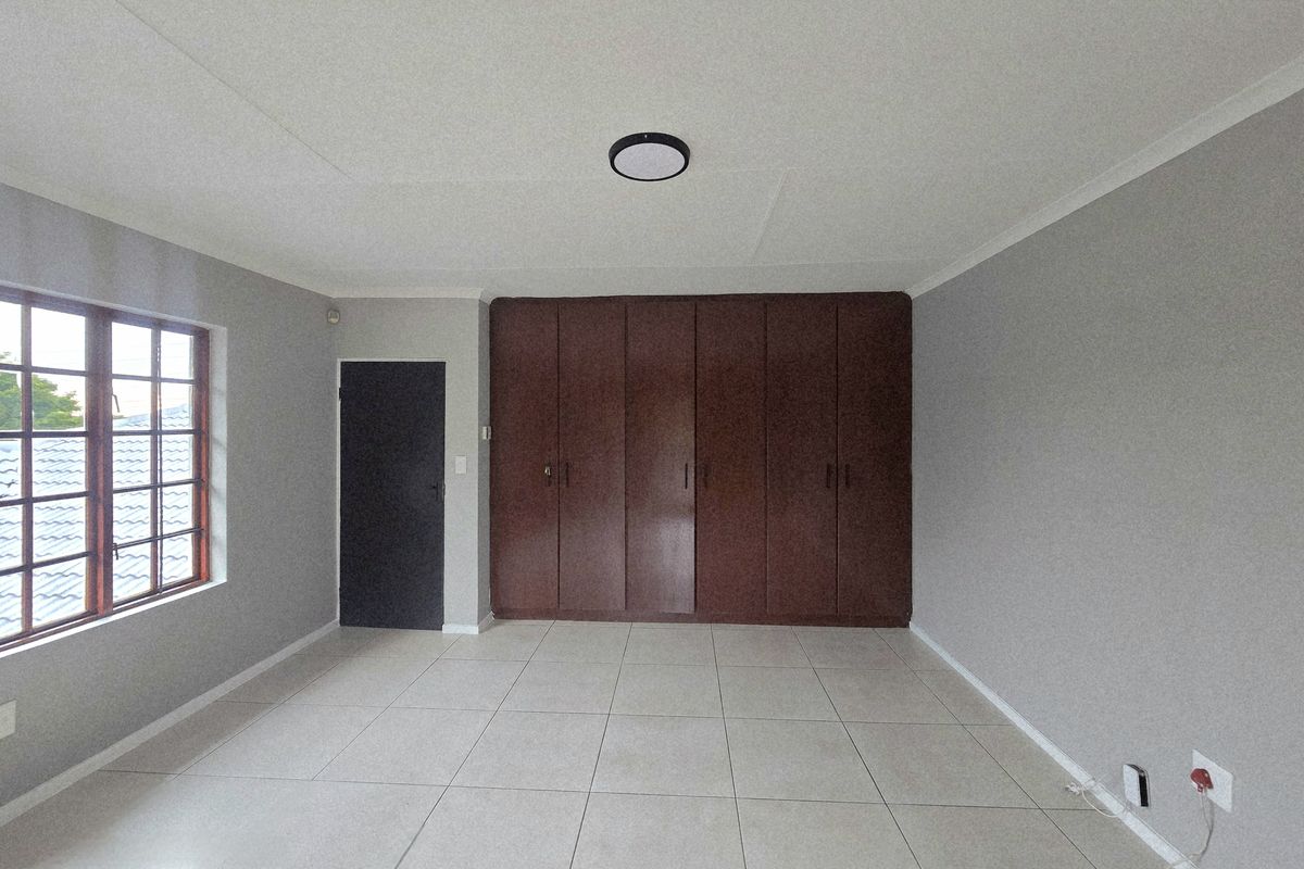 A spacious, empty bedroom featuring neutral tiled flooring, grey walls, and extensive dark wood built-in cupboards.