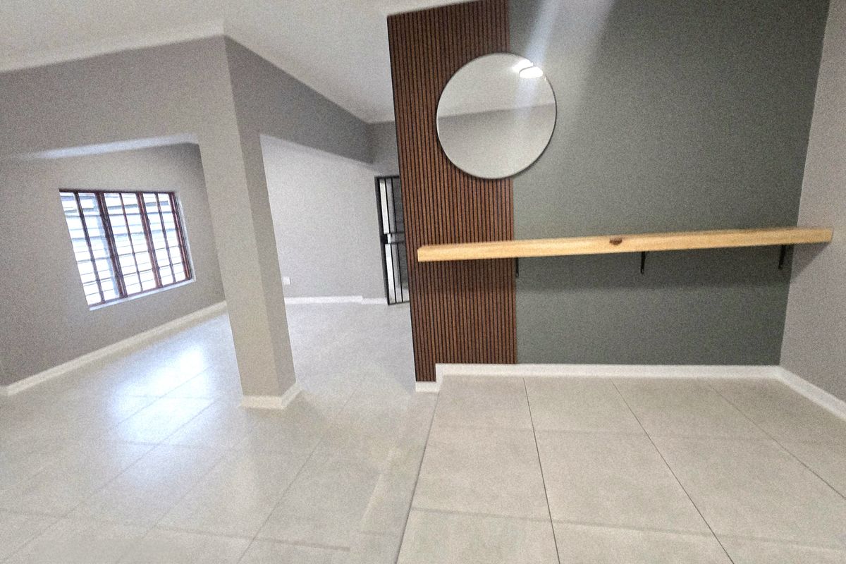 Spacious open-plan living area featuring modern tiled flooring, a decorative timber slat feature wall with a floating shelf, and secure window bars.