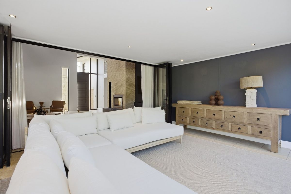 Spacious living room featuring recessed downlighting, large bi-fold doors opening to an outdoor area, and a feature fireplace visible in the adjacent space.
