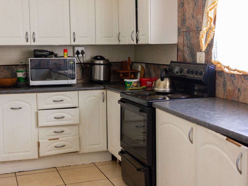 A functional kitchen featuring white cabinetry, dark laminate countertops, a tiled backsplash, and a freestanding stove with oven.