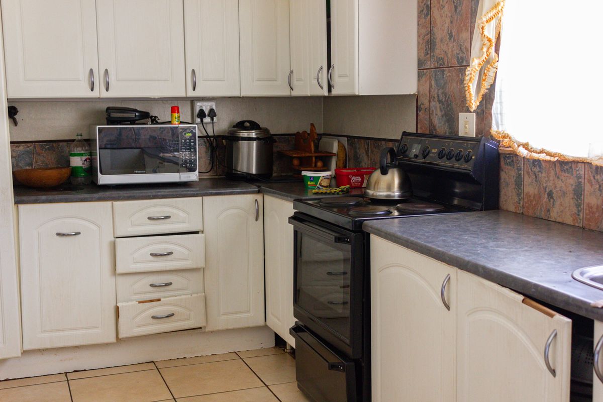 A functional kitchen featuring white cabinetry, dark laminate countertops, a tiled backsplash, and a freestanding stove with oven.