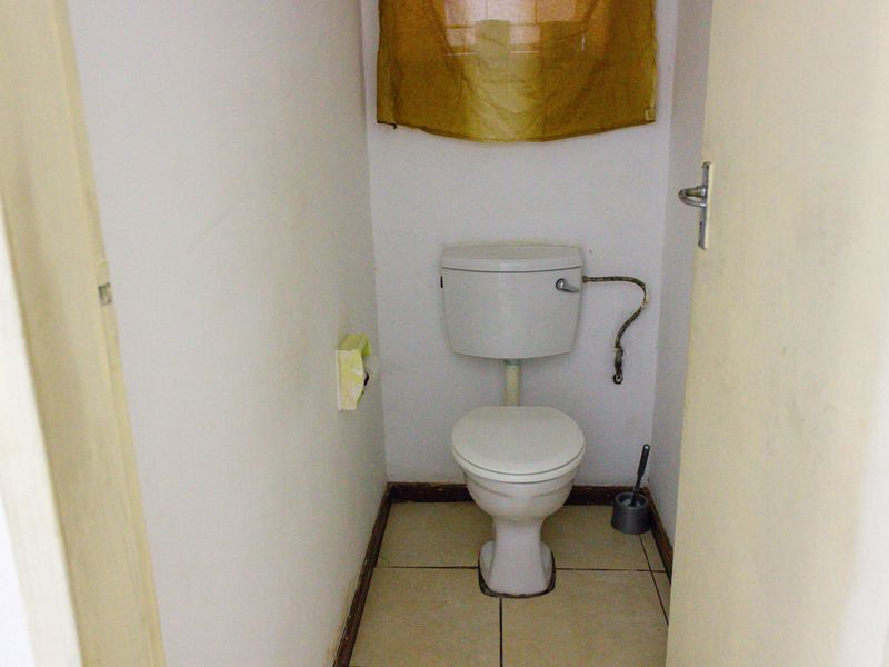 A small, functional guest toilet featuring ceramic floor tiles and standard sanitary ware, currently in need of cosmetic updates.