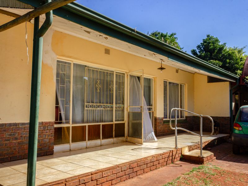 Rear exterior view of the house featuring a tiled patio area, brick foundation, and metal security gates over the windows and doors.