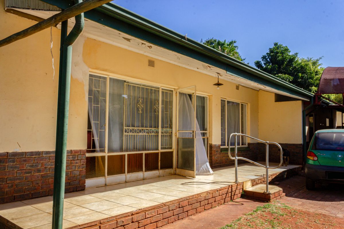 Rear exterior view of the house featuring a tiled patio area, brick foundation, and metal security gates over the windows and doors.