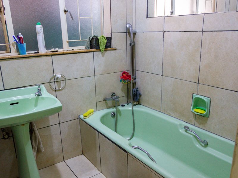 A dated bathroom featuring a green pedestal basin and matching bathtub with tiled walls and flooring, requiring modernization of fixtures and finishes.
