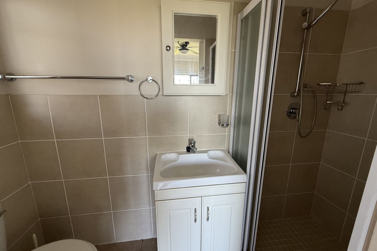 A functional bathroom featuring a vanity basin, a shower enclosure with a glass door, and tiled walls.