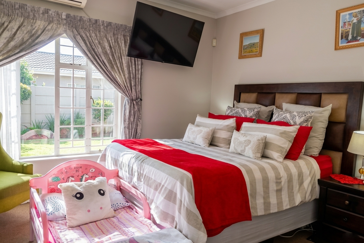 A well-maintained bedroom featuring a wall-mounted television, split-system air conditioning unit, and a window with security bars overlooking the garden.