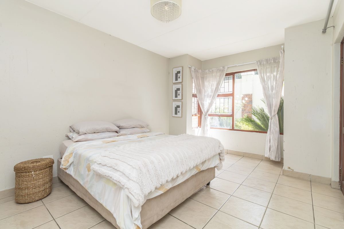 A bedroom featuring tiled flooring, a large window with security bars, and neutral wall finishes, offering a functional space with natural light.