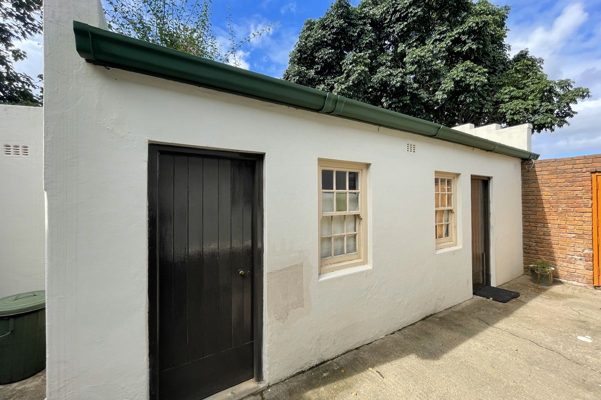 Exterior view of a utility building featuring white painted walls, dark timber door, and sash windows with a green gutter system.