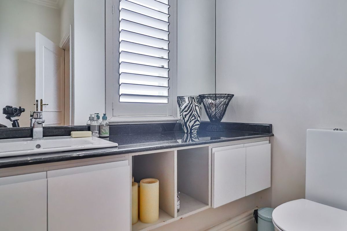 A clean bathroom featuring a vanity with a granite countertop, integrated sink, wall-mounted mirror, and shutter window for natural light.