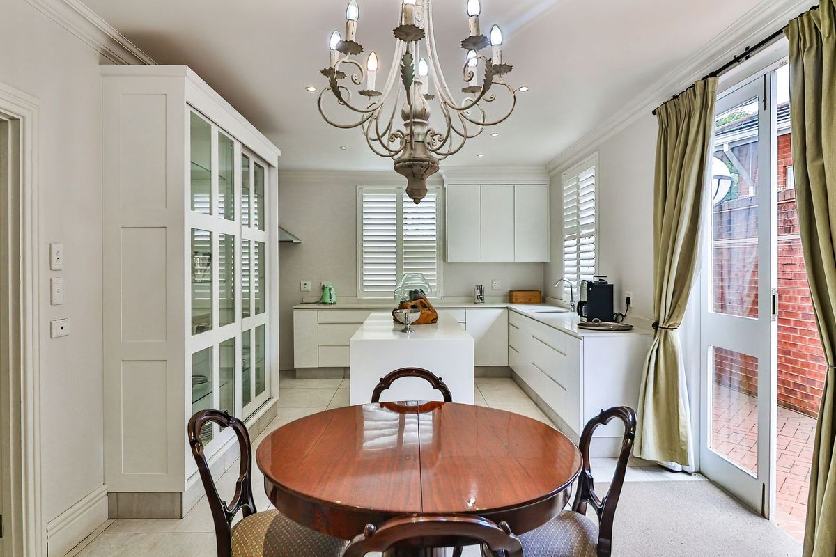 Modern white kitchen featuring a central island, ample built-in cabinetry, glass-front display unit, and plantation shutters with direct access to the outdoor area.