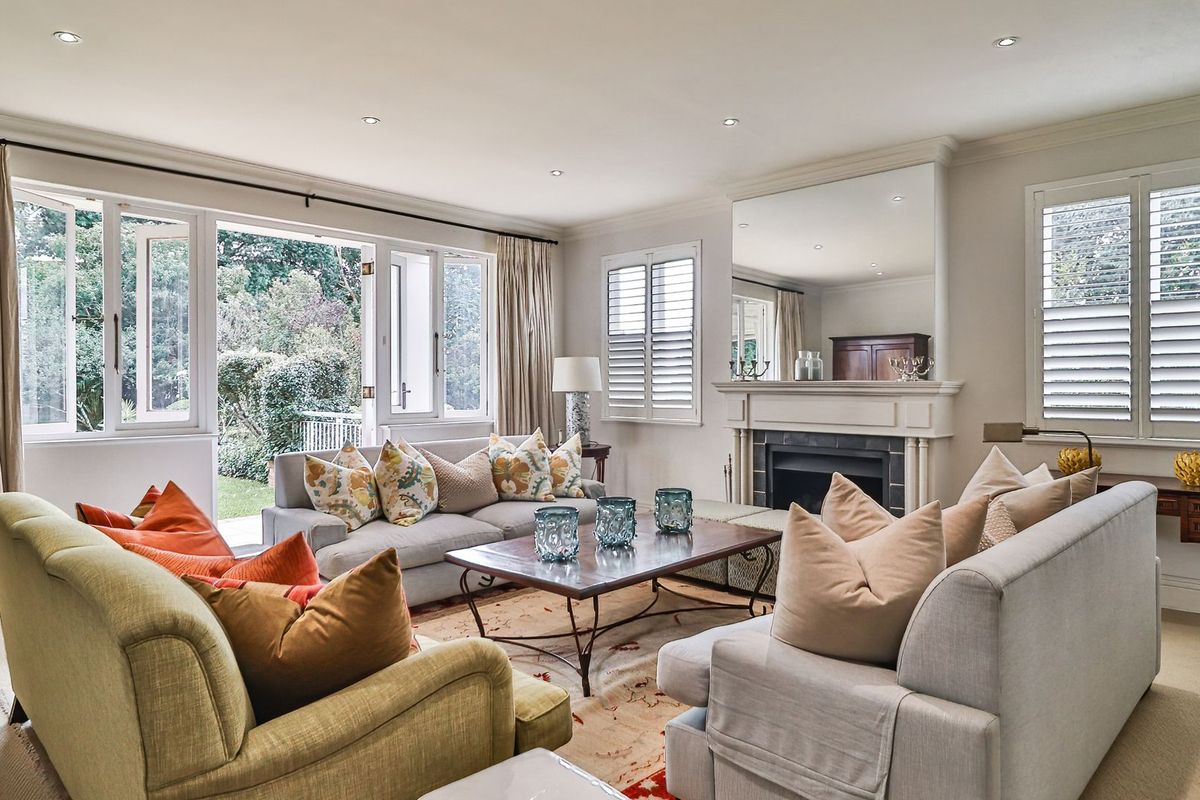 Spacious living room featuring a classic fireplace with mantel, recessed lighting, plantation shutters, and direct access to the garden through French doors.