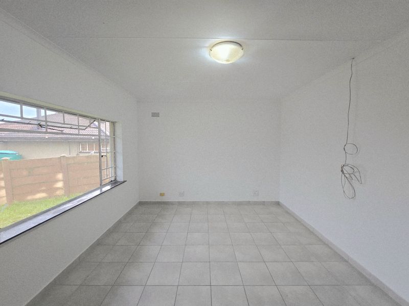A bright, empty living room featuring neutral floor tiles, a large window, and a central ceiling light fixture.