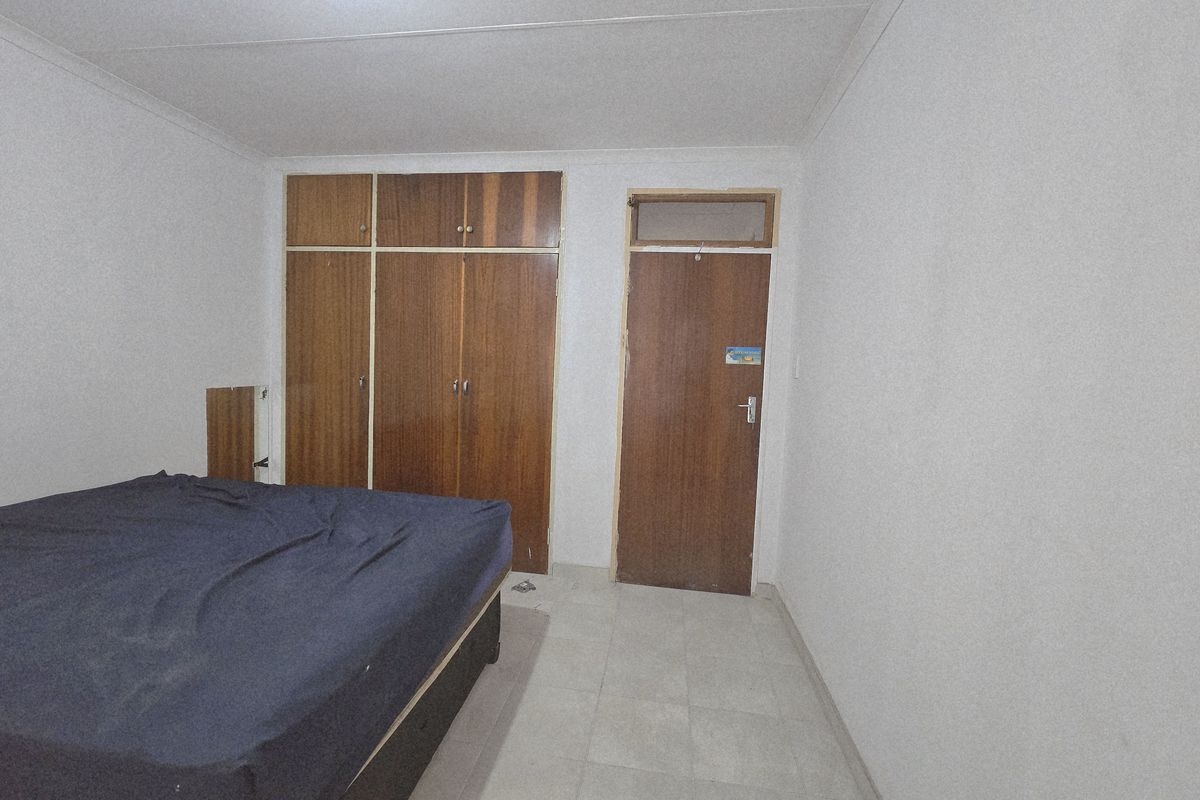 A bedroom featuring built-in wooden cupboards, tiled flooring, and a standard interior door.