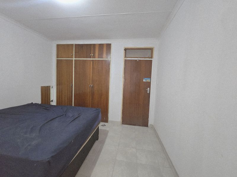 A bedroom featuring built-in wooden cupboards, tiled flooring, and a standard interior door.