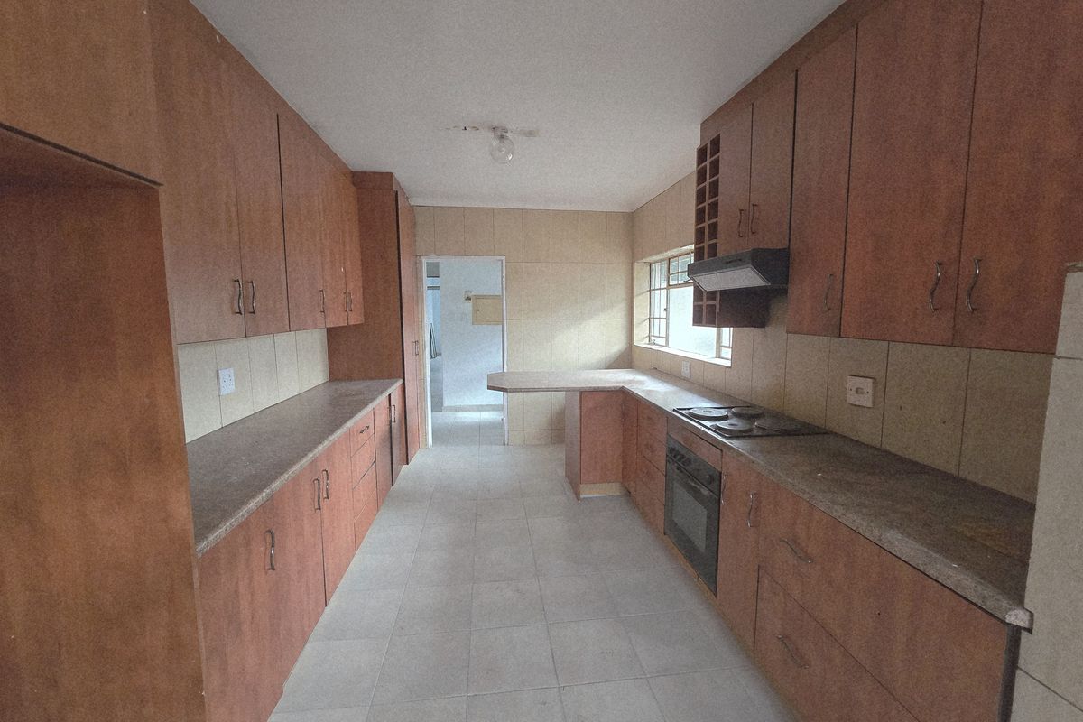 A functional galley-style kitchen featuring wood-look cabinetry, built-in oven, hob, extractor fan, and tiled flooring.