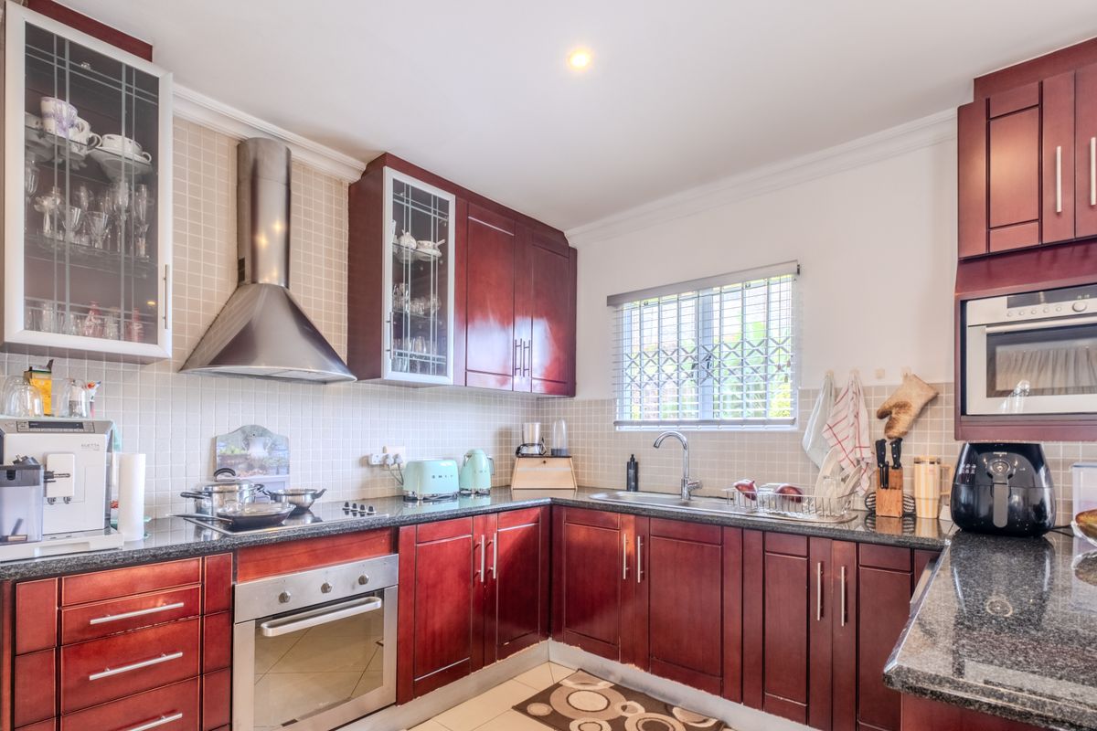 A well-maintained kitchen featuring dark wood cabinetry, granite countertops, a built-in oven, and a stainless steel extractor fan.