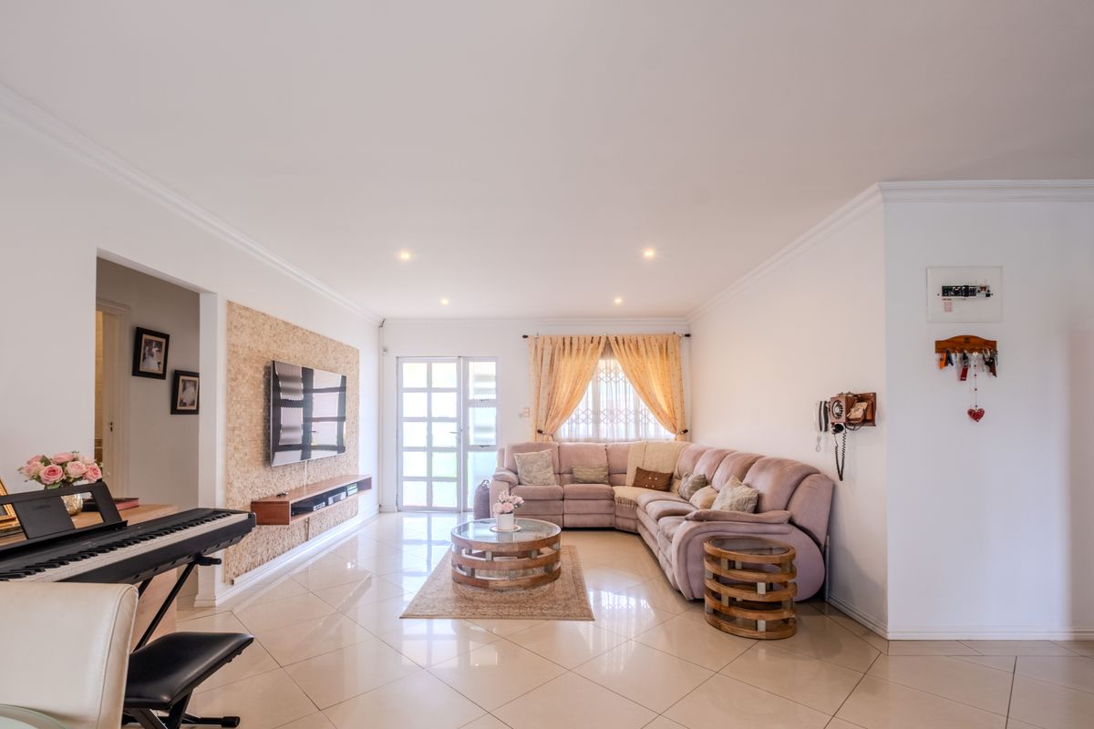A bright and spacious living room featuring polished porcelain floor tiles, a textured feature wall with a floating media console, and recessed downlighting.