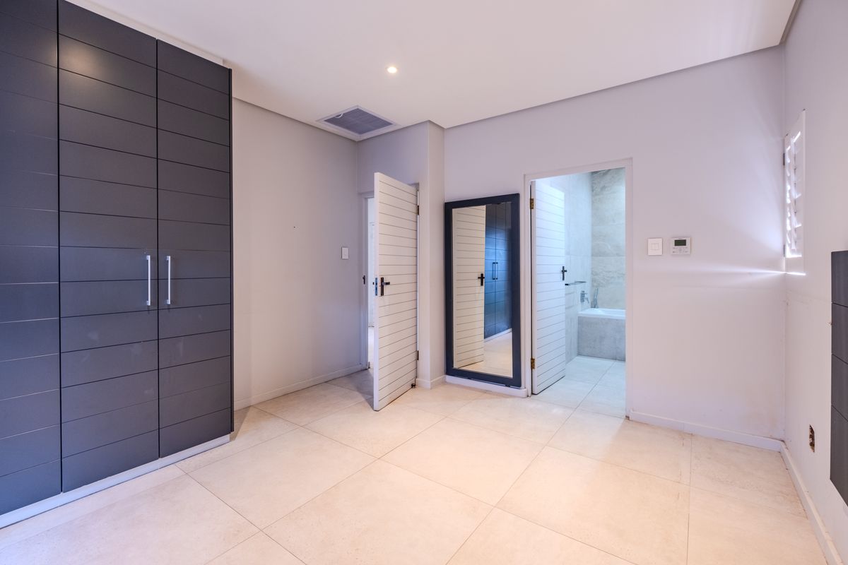 A spacious, modern bedroom featuring large built-in cupboards, neutral tiled flooring, and direct access to an en-suite bathroom.