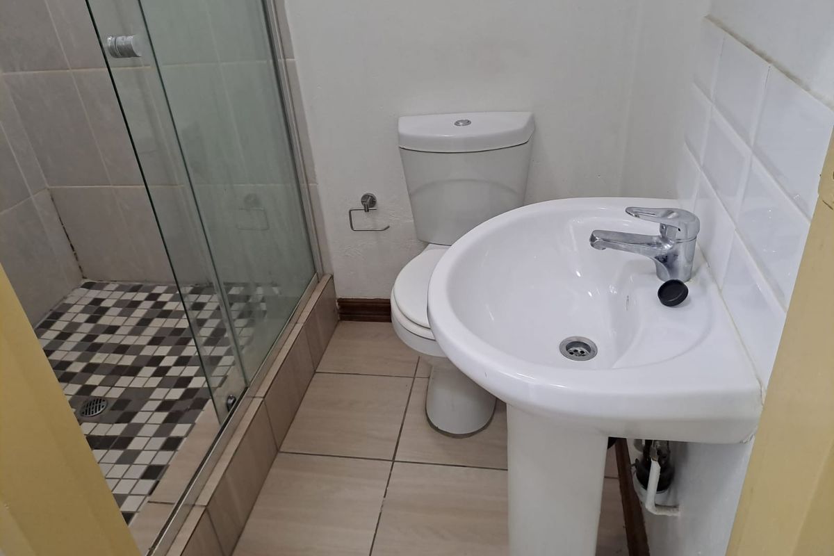 A functional bathroom featuring a pedestal basin, a glass-enclosed shower with patterned floor tiles, and standard ceramic floor tiling.