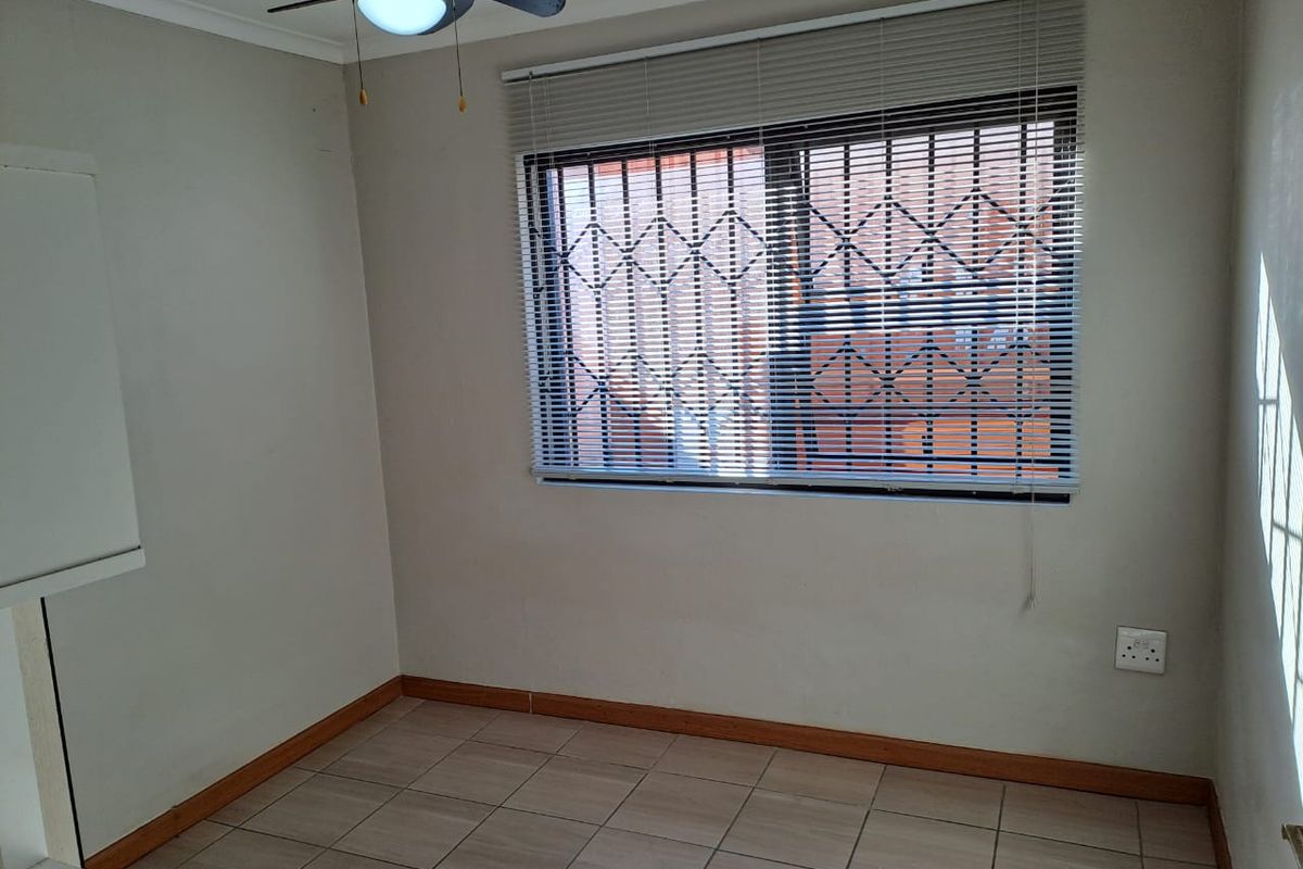 A clean, empty bedroom featuring tiled flooring, a ceiling fan, and a window fitted with security bars and venetian blinds.