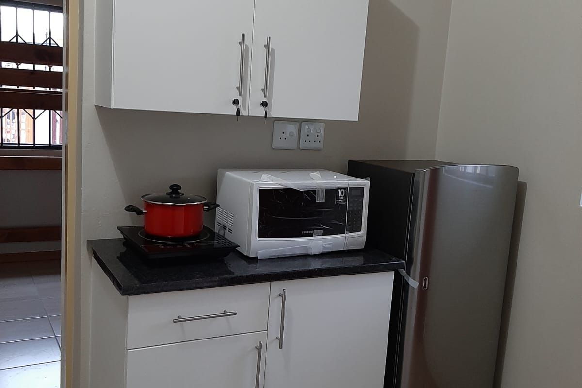 A compact kitchen area featuring white built-in cabinetry, dark granite countertops, and tiled flooring, providing a functional and clean preparation space.