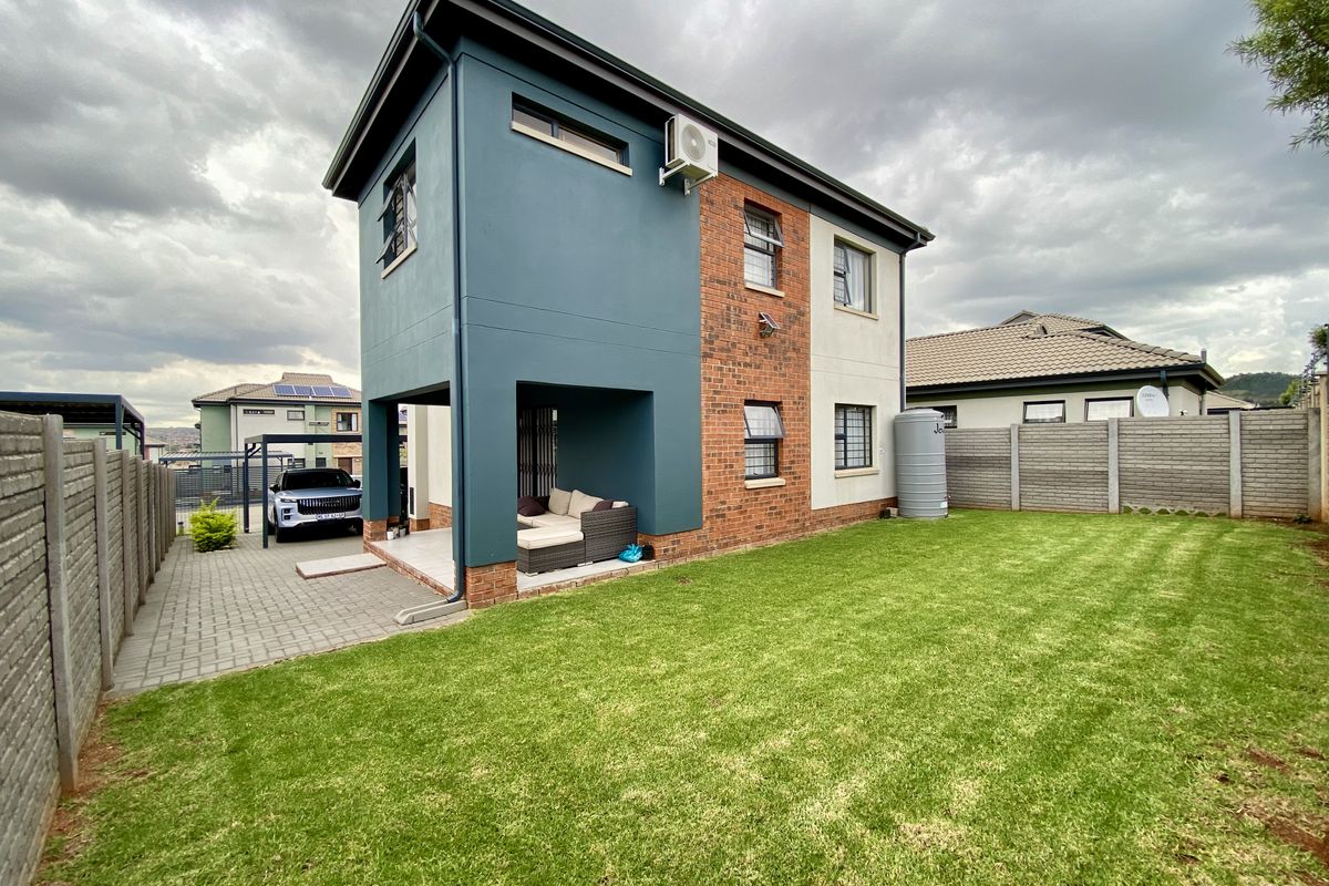 Rear view of a modern two-story home featuring a combination of brick and painted plaster finishes, a covered patio, and a well-maintained lawn.