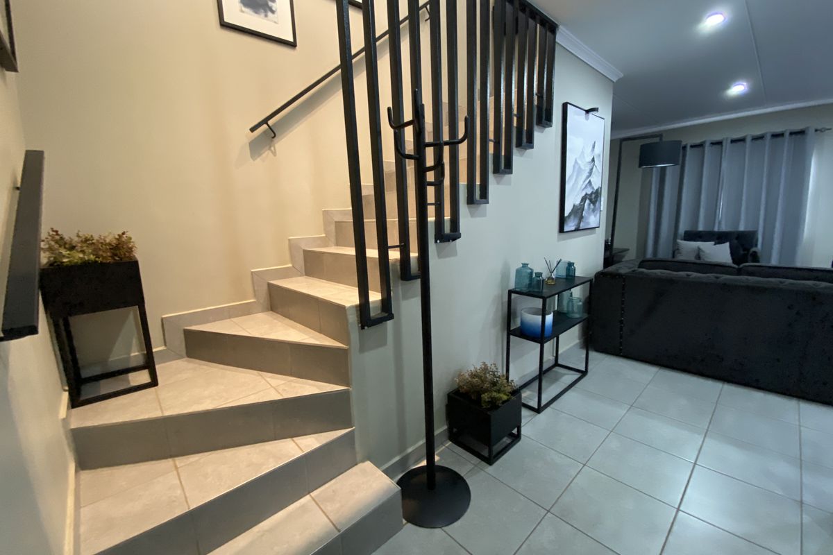 Open plan living area featuring tiled flooring, a modern staircase with a black metal balustrade, and recessed downlighting.
