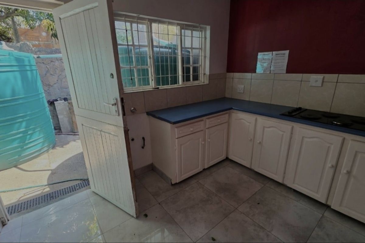 A compact kitchen featuring white built-in cabinetry, blue countertops, and an electric hob, with direct access to an outdoor area.