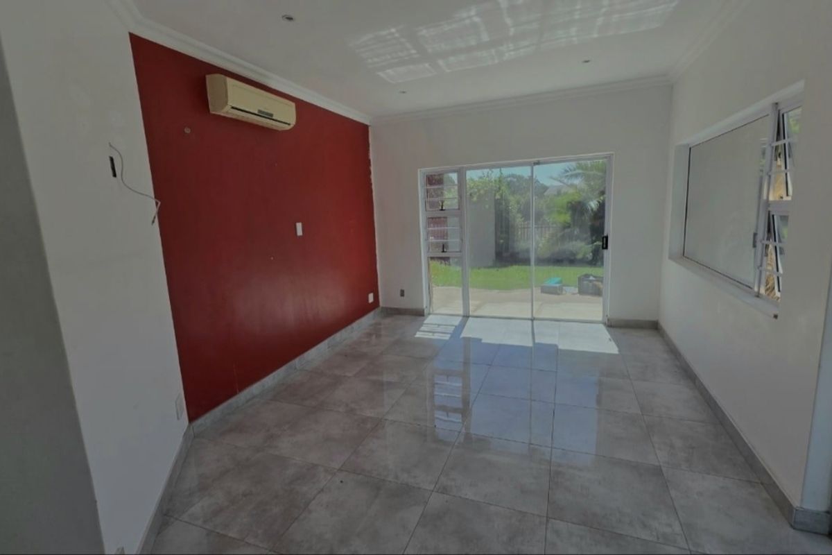 An empty living room featuring large format floor tiles, a split-system air conditioner, and sliding glass doors providing access to the rear garden.