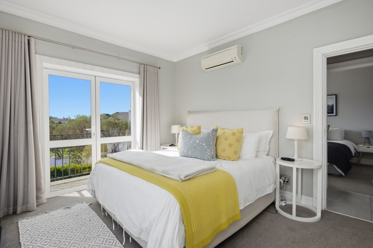 A bright and well-maintained bedroom featuring a split-system air conditioner, crown molding, and glass double doors opening onto a private balcony.