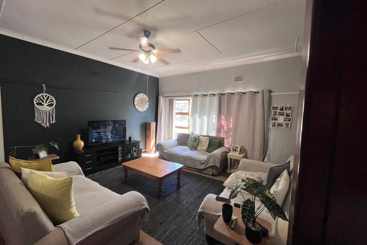 A comfortable living room featuring a dark accent wall, ceiling fan, and large windows that provide natural light.