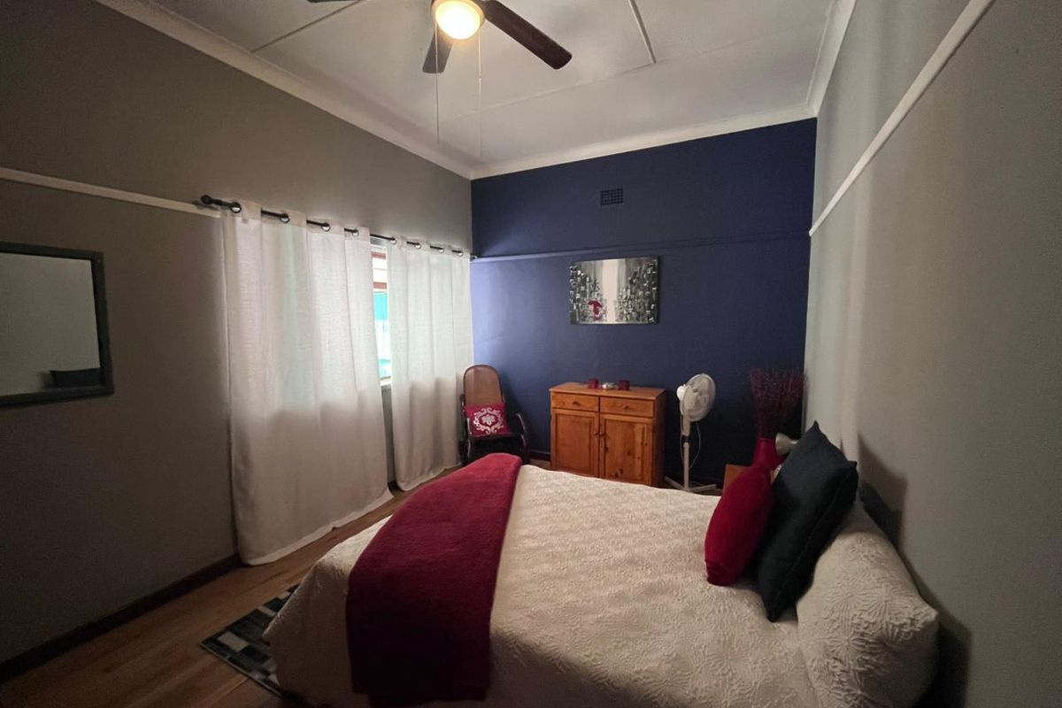 A well-proportioned bedroom featuring high ceilings, a central ceiling fan, and polished timber flooring with a contrasting dark blue feature wall.