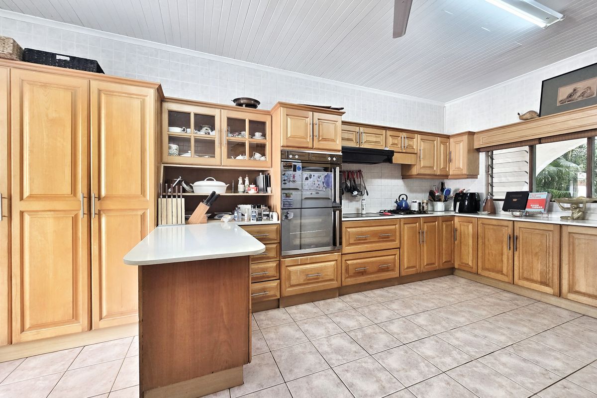 Spacious kitchen featuring extensive wooden cabinetry, built-in oven, hob with extractor fan, and tiled flooring, offering ample storage and workspace.