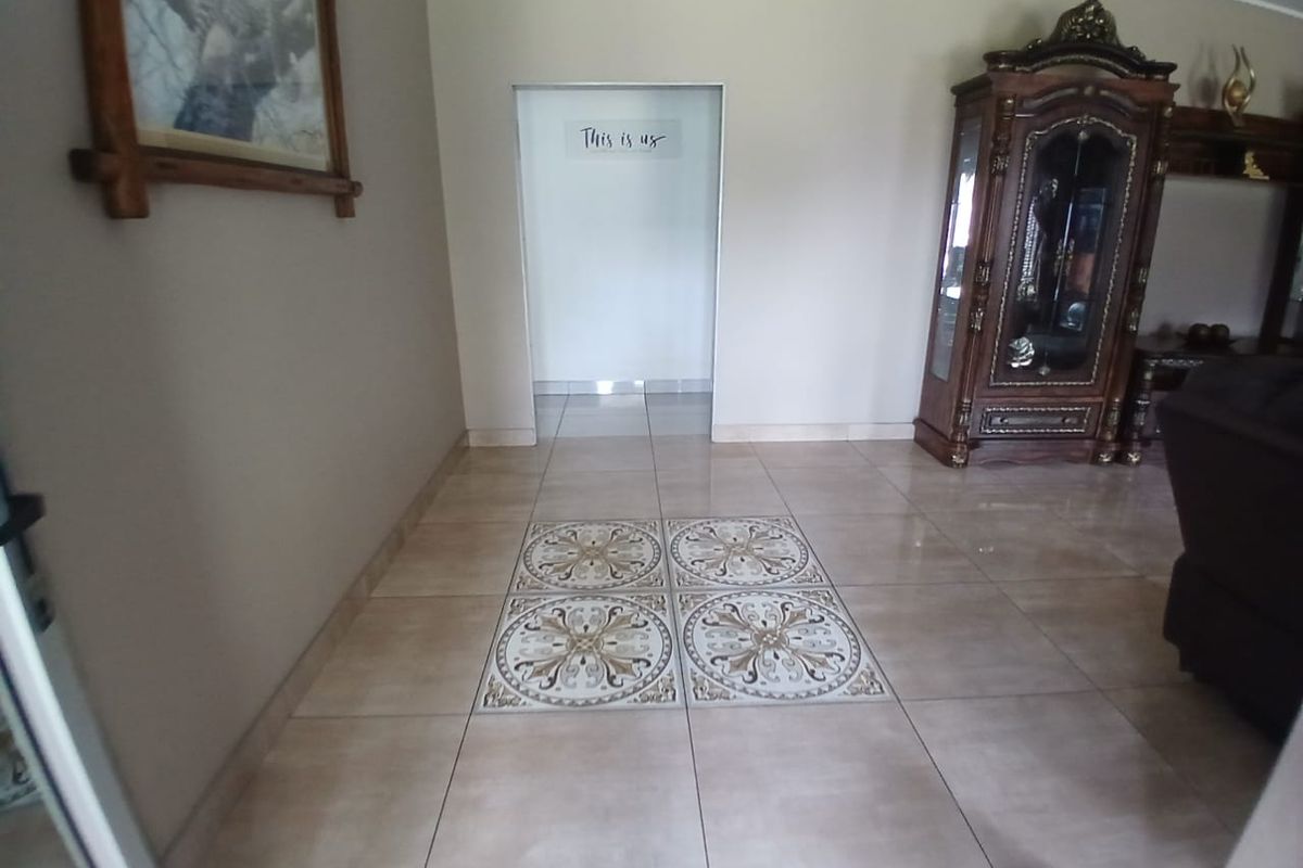 A living area featuring neutral ceramic floor tiles with a decorative central inlay, leading into an adjacent room through a wide doorway.