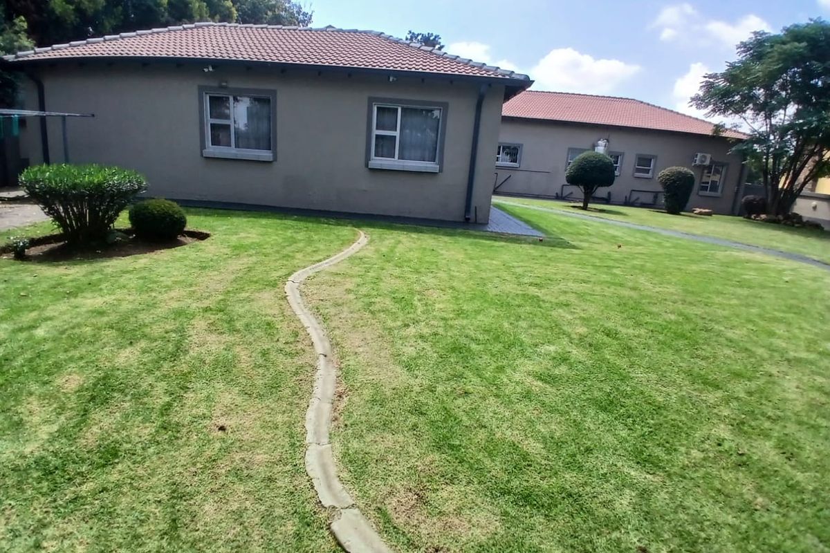 A view of the rear garden featuring a well-maintained lawn, concrete pathway, and the rear elevation of the house with a tiled roof.