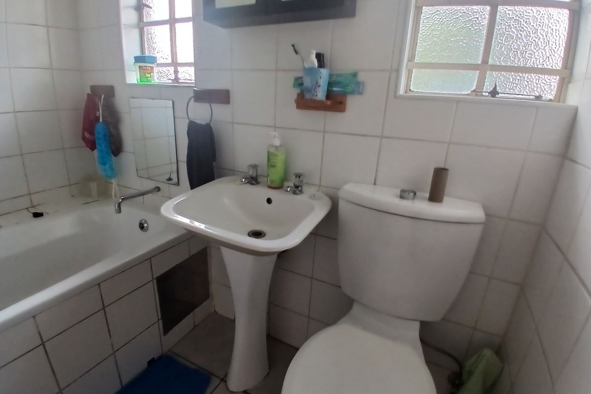 A dated bathroom featuring a pedestal basin, toilet, and bathtub with white wall tiles and obscured glass windows.