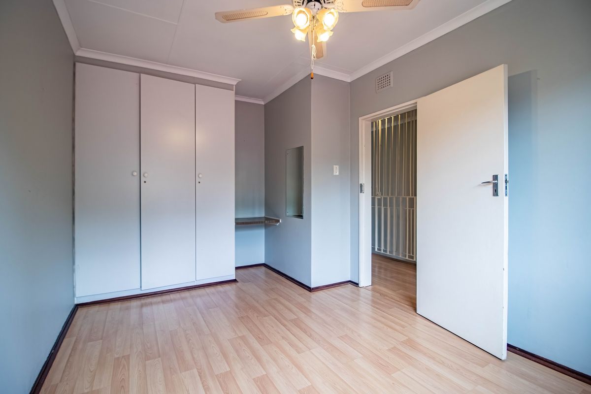 A bright, empty bedroom featuring laminate flooring, built-in cupboards, and a ceiling fan, providing a clean and neutral space ready for personalization.