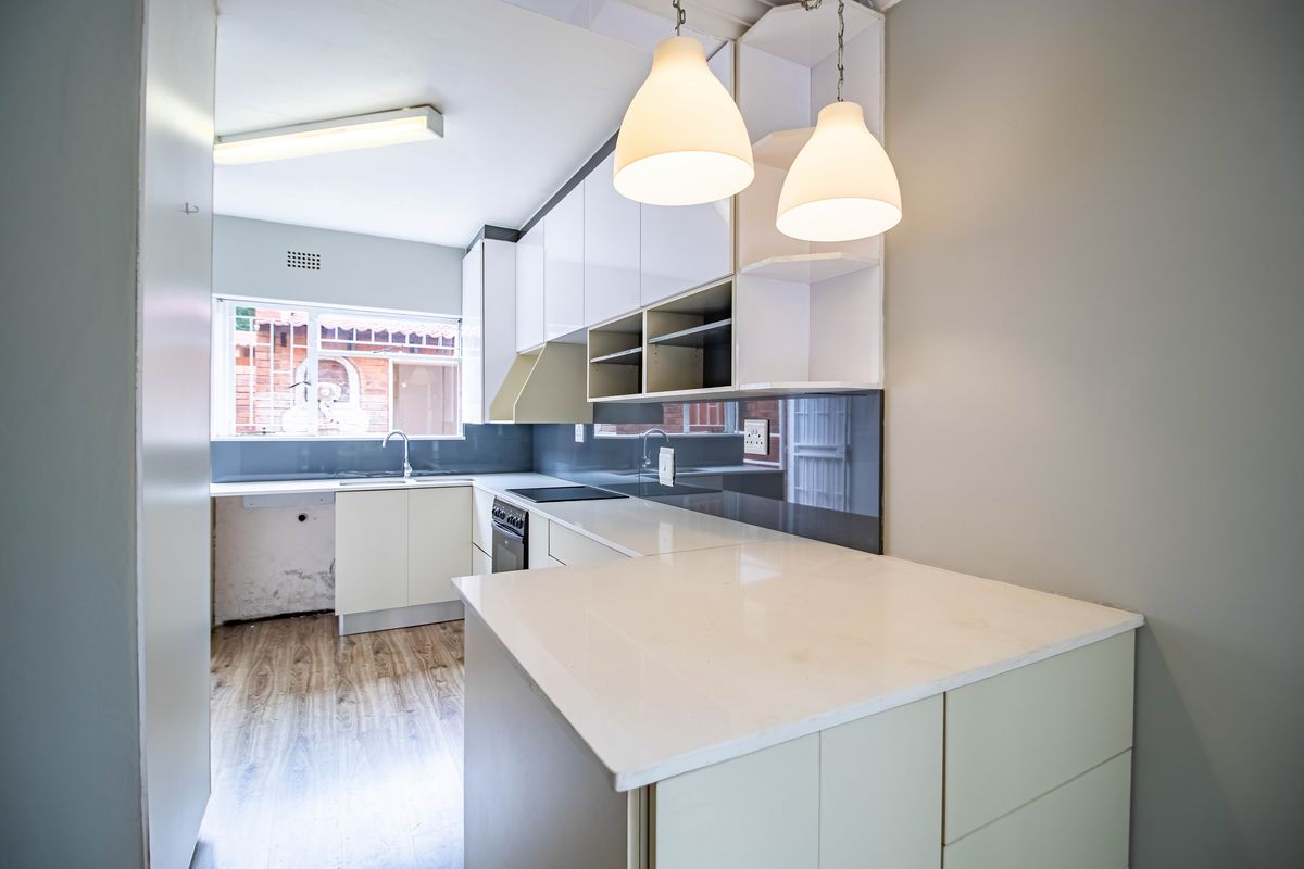 Modern kitchen featuring white cabinetry, stone countertops, glass splashbacks, and integrated appliances, offering a clean and functional workspace.