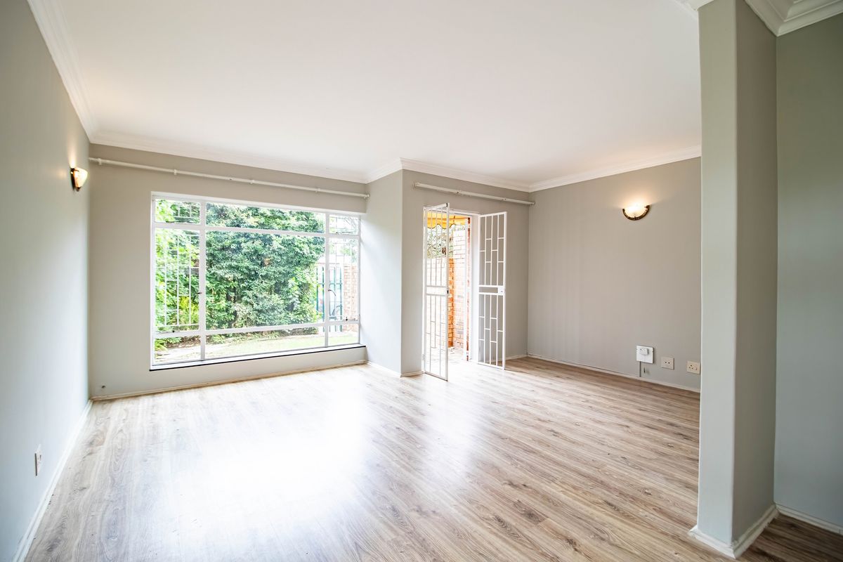 A bright and spacious living area featuring modern laminate flooring, large windows, and direct access to the exterior through a security gate.