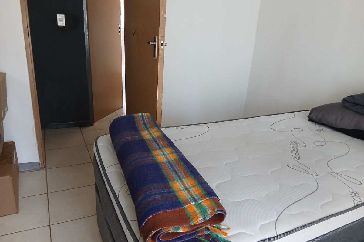 A bedroom interior featuring tiled flooring and a doorway leading to an adjacent space.